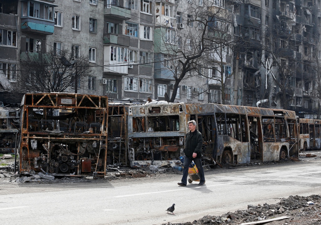 A local resident walks along a street in front of burnt-out buses during the Ukraine-Russia conflict in the southern port city of Mariupol.